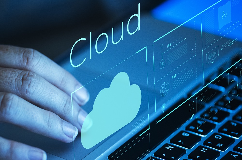 Mão sobre o teclado de um notebook com a figura de uma nuvem, representando o banco de dados na nuvem